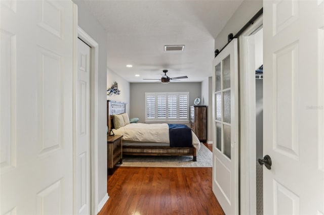 bedroom with ceiling fan, a barn door, and dark wood-type flooring