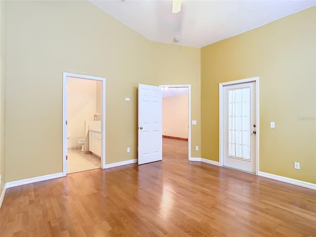 unfurnished bedroom featuring a high ceiling, ensuite bath, ceiling fan, and light hardwood / wood-style floors