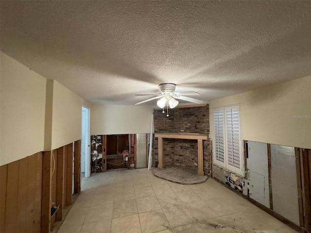 unfurnished living room featuring ceiling fan, wooden walls, and a textured ceiling