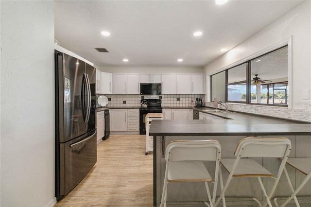 kitchen featuring black appliances, a breakfast bar area, white cabinets, kitchen peninsula, and light hardwood / wood-style flooring