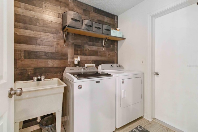 laundry room with wood walls, sink, washer and clothes dryer, a textured ceiling, and light wood-type flooring