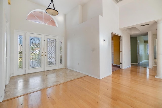 foyer with a high ceiling, light hardwood / wood-style floors, and french doors