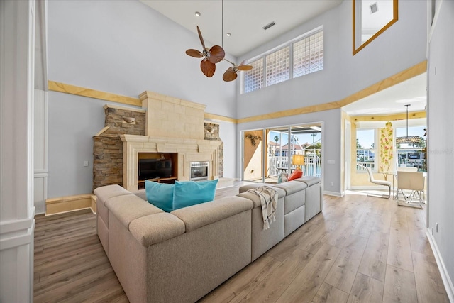 living room with a high ceiling, ceiling fan, light wood-type flooring, and a fireplace