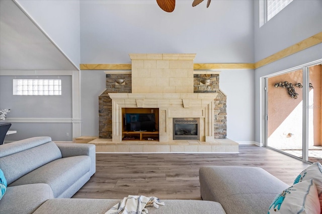 living room with a tiled fireplace, a towering ceiling, plenty of natural light, and light hardwood / wood-style flooring