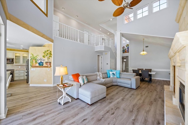 living room with a high ceiling, ornamental molding, ceiling fan, a premium fireplace, and light wood-type flooring