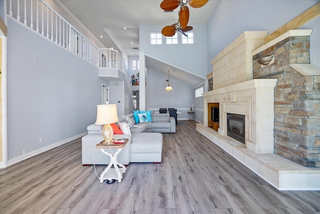 living room with ceiling fan, hardwood / wood-style floors, a tile fireplace, and a towering ceiling