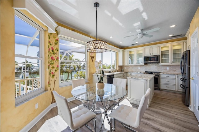 dining space featuring sink, light hardwood / wood-style flooring, ceiling fan, and a water view