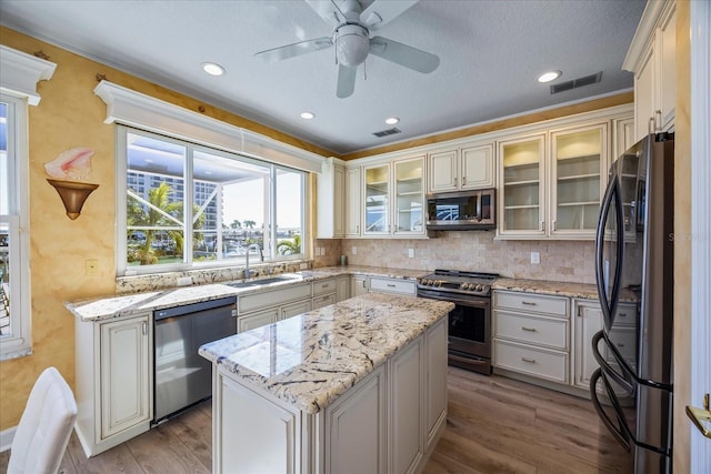 kitchen featuring sink, stainless steel appliances, light hardwood / wood-style floors, light stone countertops, and a kitchen island