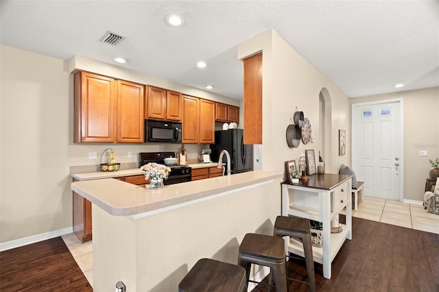 kitchen featuring a textured ceiling, light tile patterned flooring, kitchen peninsula, a breakfast bar area, and black appliances