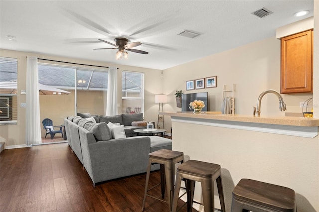 living room with a textured ceiling, ceiling fan, and dark wood-type flooring