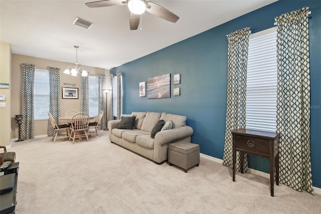 carpeted living room with ceiling fan with notable chandelier