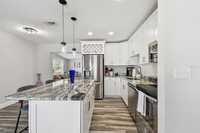 kitchen featuring a kitchen island, white cabinetry, stainless steel appliances, sink, and a breakfast bar