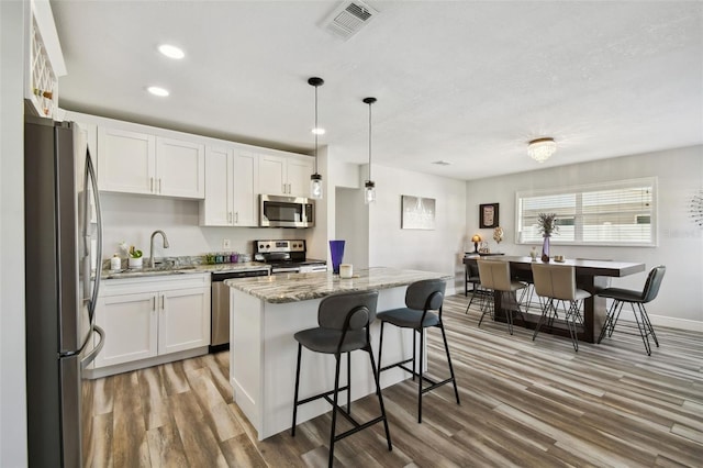 kitchen featuring stainless steel appliances, hanging light fixtures, a kitchen island, white cabinets, and sink