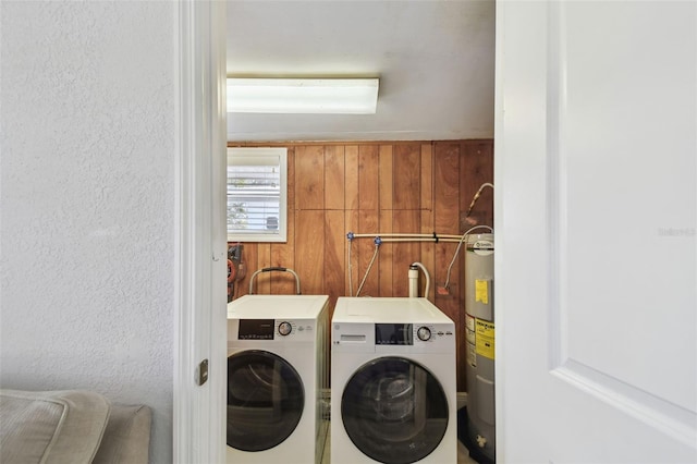 laundry room with electric water heater, wood walls, and washing machine and clothes dryer