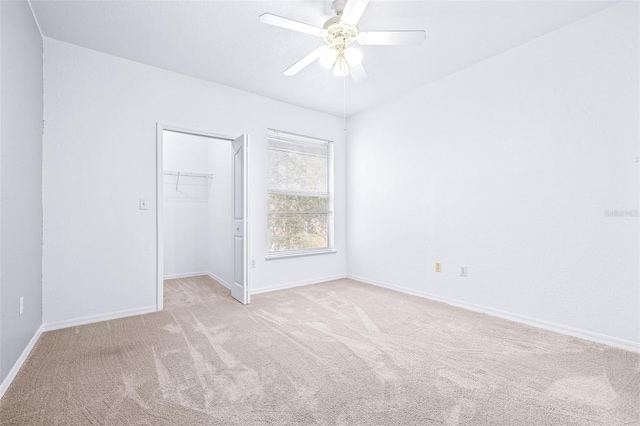 unfurnished bedroom with ceiling fan, a walk in closet, a closet, and light colored carpet