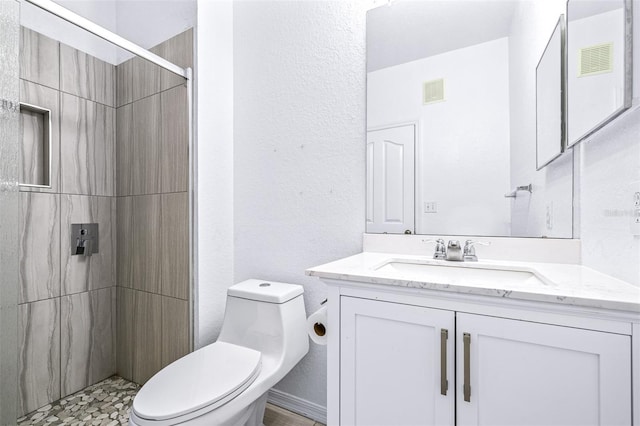 bathroom featuring toilet, a tile shower, and vanity