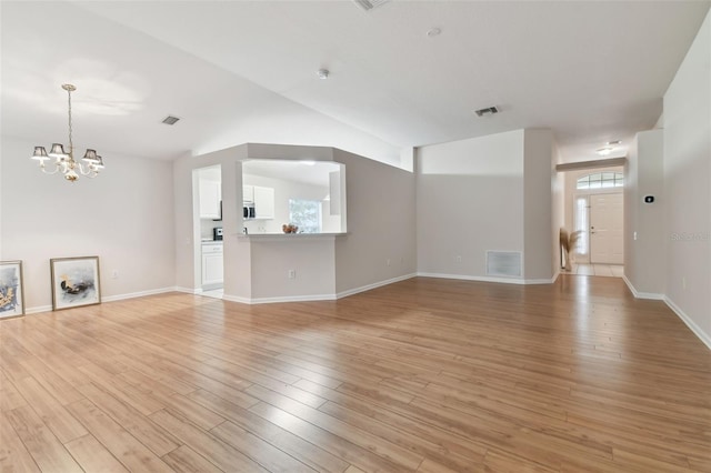 unfurnished living room featuring lofted ceiling, an inviting chandelier, and light hardwood / wood-style floors