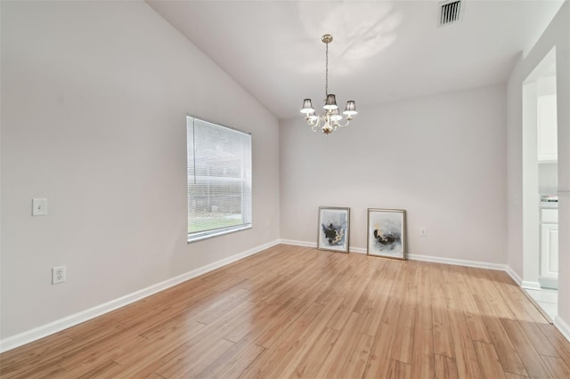 spare room featuring lofted ceiling, a chandelier, and light wood-type flooring