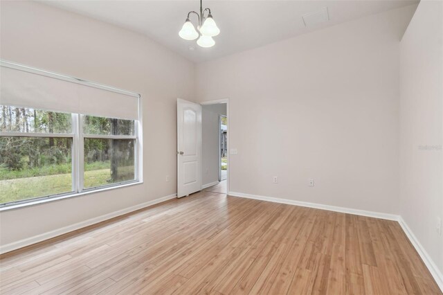 spare room with an inviting chandelier, a healthy amount of sunlight, and light wood-type flooring