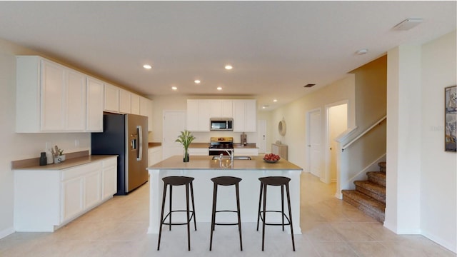 kitchen featuring stainless steel appliances, a kitchen island with sink, white cabinets, light tile patterned flooring, and sink