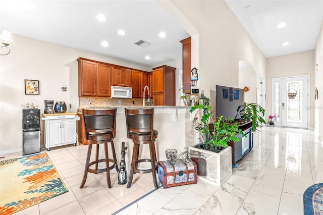 kitchen with kitchen peninsula, backsplash, light stone counters, and a kitchen bar