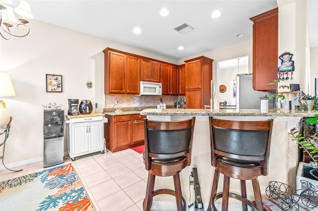 kitchen with kitchen peninsula, light tile patterned floors, a kitchen bar, and light stone counters