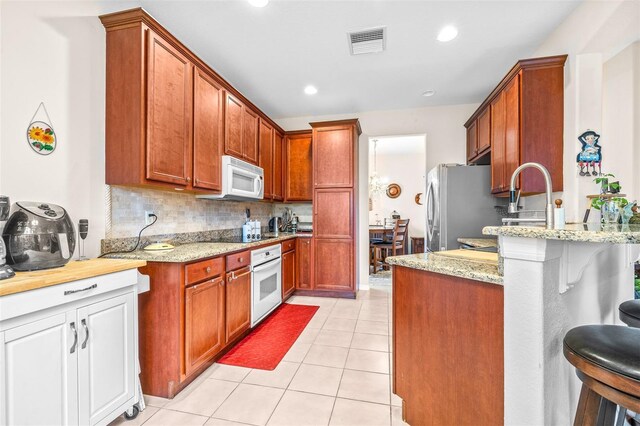 kitchen with white appliances, backsplash, kitchen peninsula, light stone counters, and a breakfast bar area