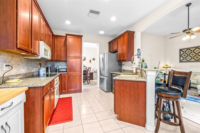 kitchen featuring ceiling fan, white appliances, light stone counters, a breakfast bar, and sink