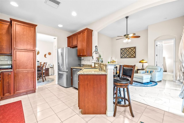 kitchen featuring ceiling fan, kitchen peninsula, sink, appliances with stainless steel finishes, and light stone counters