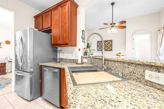 kitchen featuring appliances with stainless steel finishes, sink, light tile patterned flooring, ceiling fan, and light stone counters