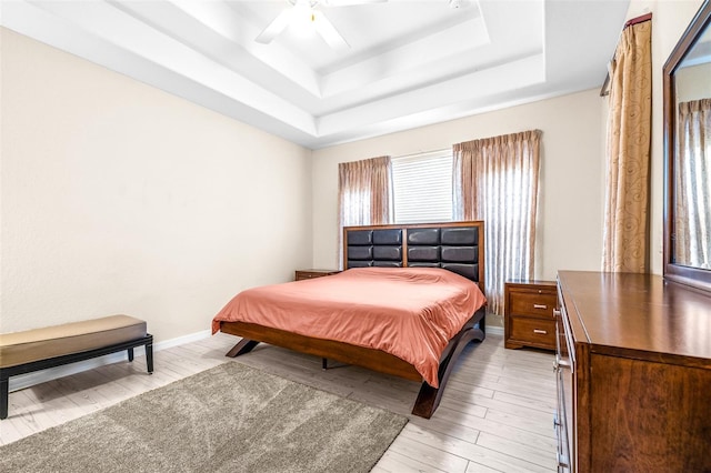 bedroom with ceiling fan, light hardwood / wood-style floors, and a raised ceiling