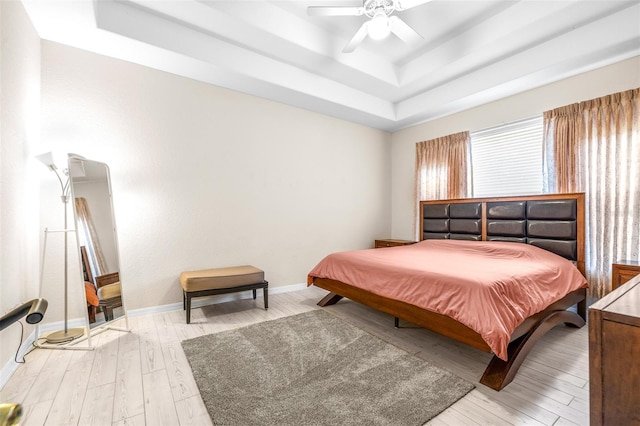 bedroom with light wood-type flooring, ceiling fan, and a tray ceiling