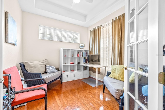 living area with hardwood / wood-style flooring, a tray ceiling, and ceiling fan