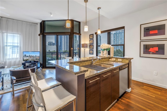 kitchen with a center island with sink, stainless steel dishwasher, sink, light stone countertops, and dark brown cabinets