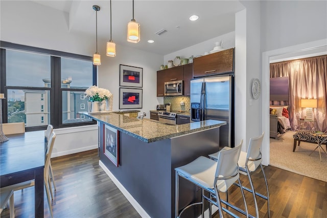 kitchen with decorative light fixtures, tasteful backsplash, stone counters, appliances with stainless steel finishes, and a breakfast bar area