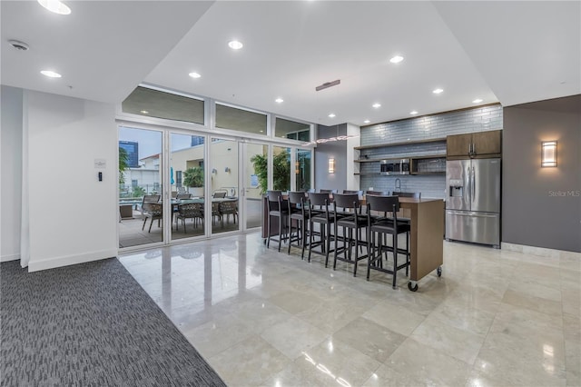 kitchen with stainless steel fridge with ice dispenser, a breakfast bar area, french doors, expansive windows, and a center island