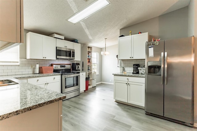 kitchen with light stone countertops, appliances with stainless steel finishes, white cabinetry, and pendant lighting