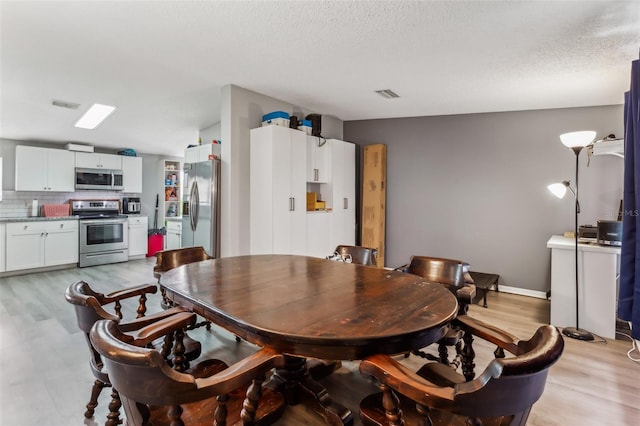 dining space with light wood-type flooring and a textured ceiling