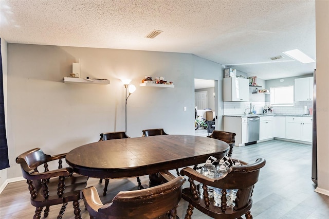 dining area featuring vaulted ceiling with skylight, hardwood / wood-style floors, and a textured ceiling