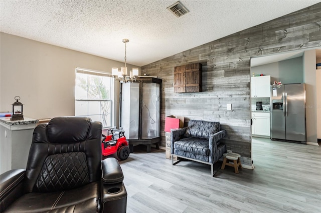 sitting room featuring wooden walls, a textured ceiling, vaulted ceiling, a chandelier, and light hardwood / wood-style flooring