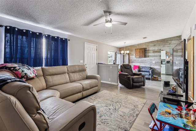 living room featuring vaulted ceiling, ceiling fan with notable chandelier, a textured ceiling, and light hardwood / wood-style flooring