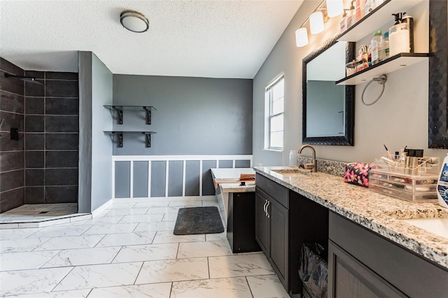 bathroom featuring a textured ceiling, tiled shower, and vanity