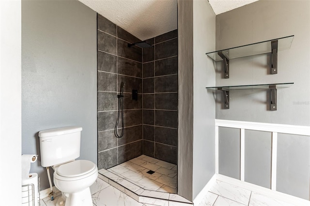 bathroom featuring a textured ceiling, toilet, and tiled shower