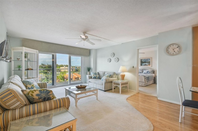 living room with a textured ceiling, ceiling fan, and light hardwood / wood-style flooring