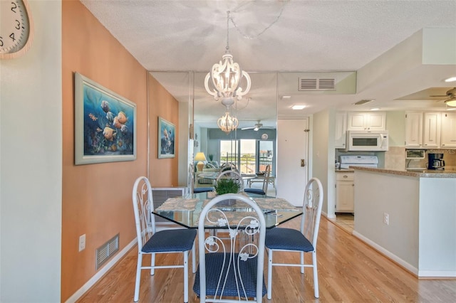 dining area with a textured ceiling, ceiling fan with notable chandelier, and light hardwood / wood-style flooring