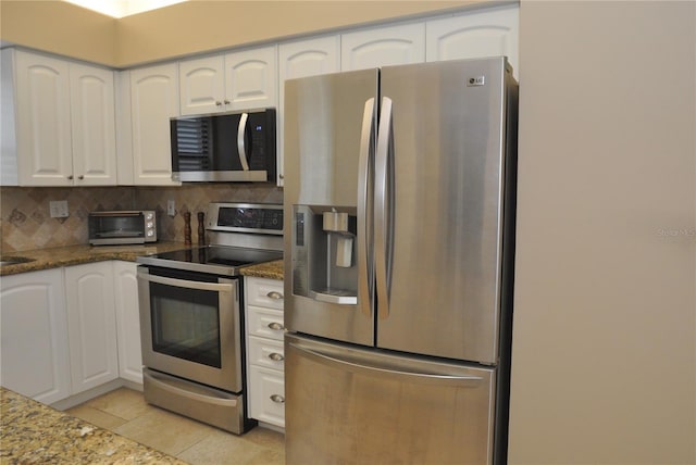 kitchen featuring white cabinets, dark stone countertops, appliances with stainless steel finishes, and light tile patterned flooring