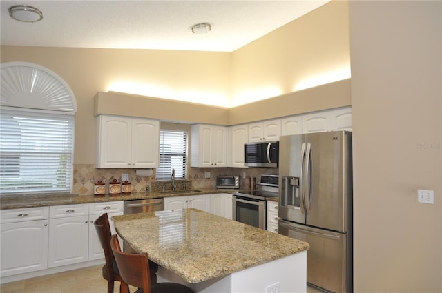 kitchen featuring light stone countertops, white cabinets, appliances with stainless steel finishes, a kitchen island, and sink