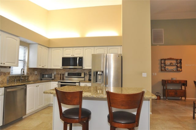 kitchen featuring white cabinets, appliances with stainless steel finishes, stone counters, and a breakfast bar area