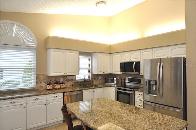 kitchen with sink, backsplash, white cabinets, dark stone counters, and stainless steel appliances