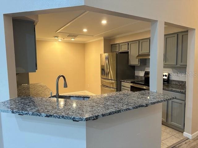 kitchen featuring kitchen peninsula, dark stone counters, ornamental molding, stainless steel refrigerator with ice dispenser, and sink